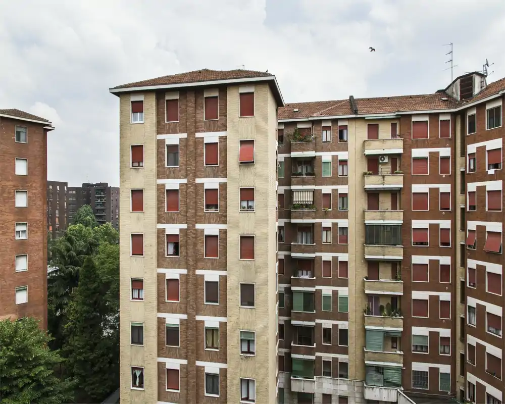 Exterior view of multiple apartment buildings with rows of windows and balconies; urban residential façade seen from across the courtyard.