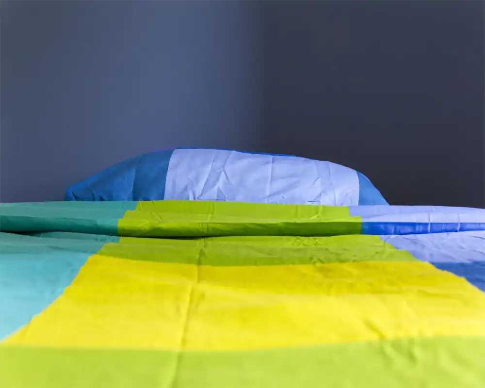 Colorful, minimal bedroom shot showing the bed made with vibrant yellow, green and blue linens against a plain dark wall — bright, sharp image ideal for listing the sleeping area.
