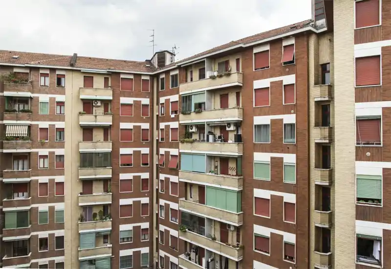 Exterior view of a multi-storey residential building showing balconies, windows and shutters facing an inner courtyard.