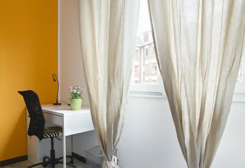 Bright, modern workspace corner with a white desk, ergonomic chair and light-filtering curtains creating a calm, airy atmosphere.