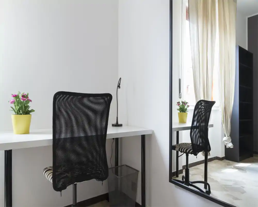 Bright, minimal workspace with a white desk, mesh office chair and potted plants beside a window; neutral tones and natural light create a clean, functional corner ideal for working or studying.