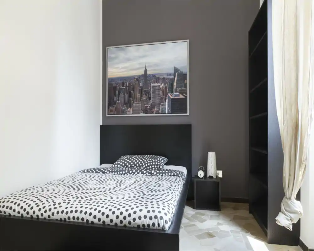 Bright, modern bedroom with a black platform bed dressed in polka-dot bedding, a framed cityscape above the headboard and a tall open shelf by the window.