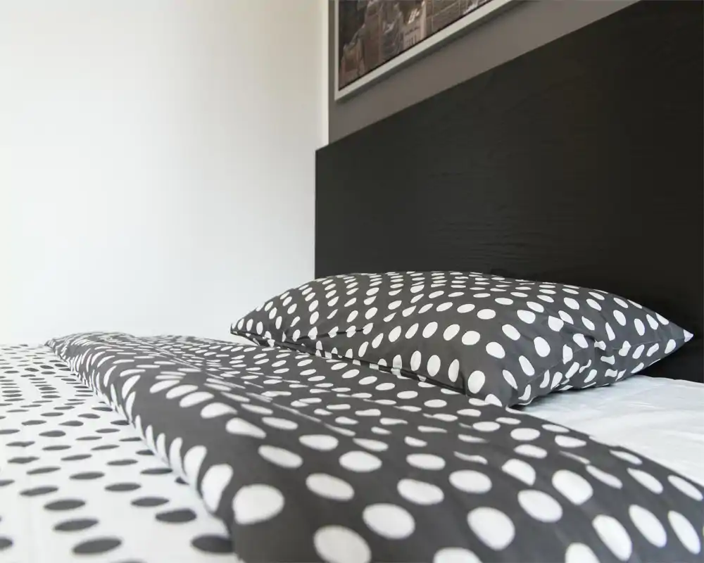 Bright, modern bedroom close-up showing a polka-dot duvet and pillows against a dark headboard — a clean, stylish sleeping area ideal for rental listings.