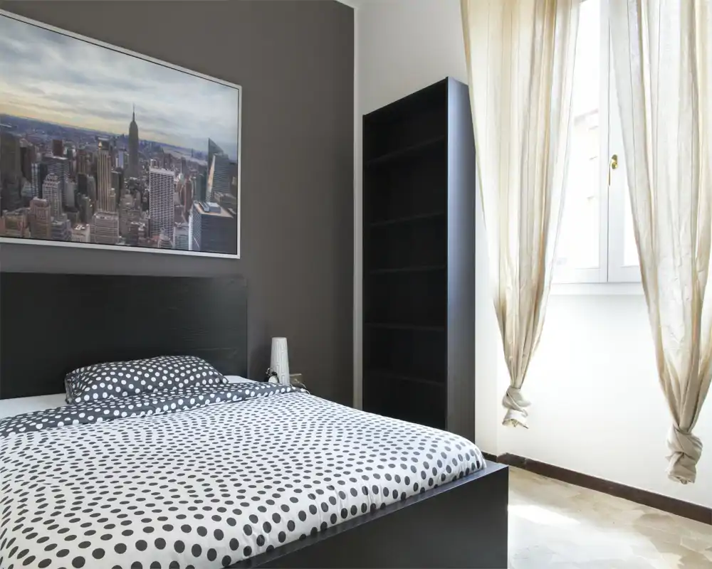 Bright, modern bedroom with a polka-dot duvet, dark headboard and a large window that fills the room with natural light. Simple shelving and neutral decor create a calm, contemporary atmosphere ideal for rental listings.