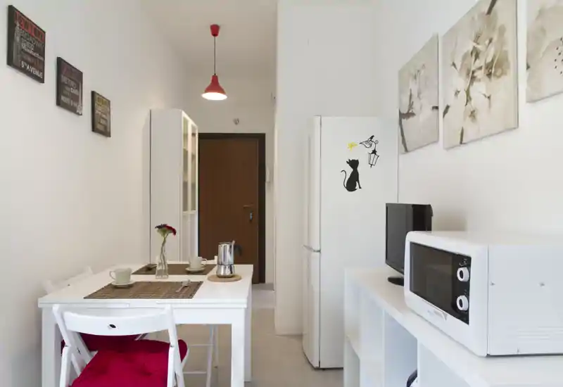 Compact, bright kitchenette with a small dining table, fridge, microwave and minimal decorative touches — ideal for a cozy studio.