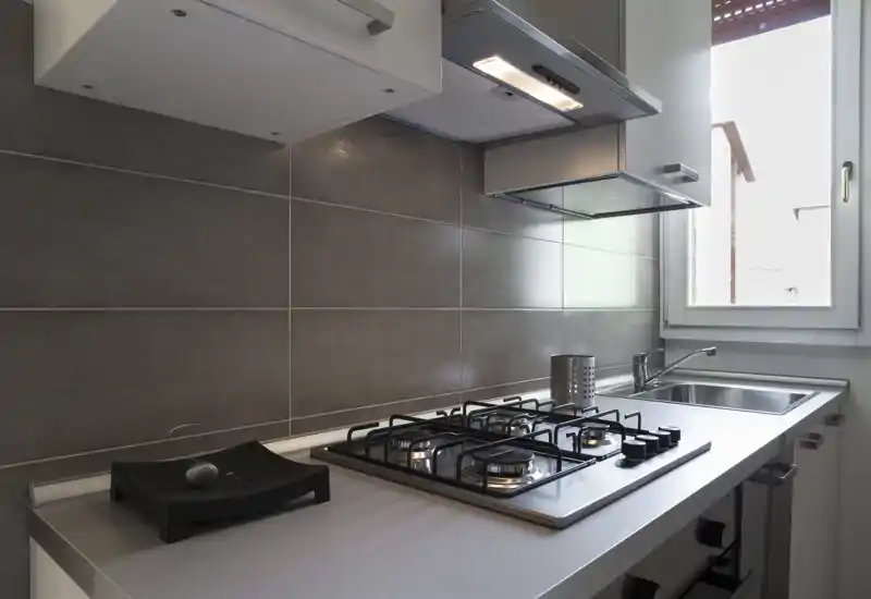 Bright, modern kitchen corner with a gas hob, stainless sink, extractor hood and tiled splashback. Clean, minimal styling and natural light from a nearby window.