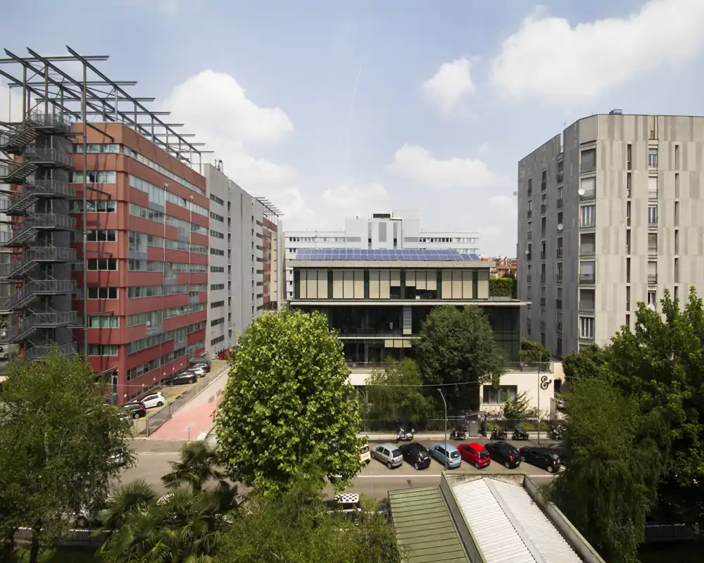 City exterior view with modern buildings, trees and parked cars under a bright blue sky — suitable as an exterior/urban listing photo.