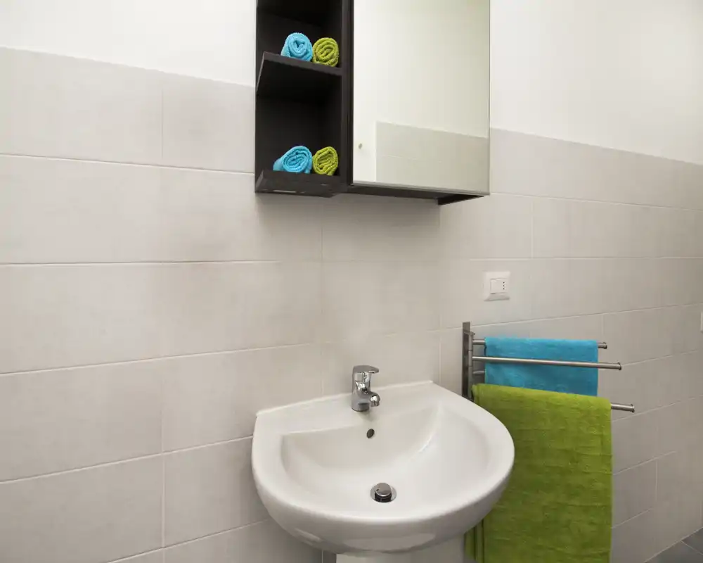 Bright, modern bathroom sink area with a white pedestal basin, chrome faucet, mirrored cabinet and colorful towels for a fresh look.