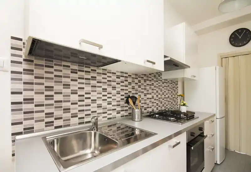 Modern compact kitchen with stainless steel sink, gas hob and mosaic tile backsplash; bright, clean and efficiently arranged for city apartments.