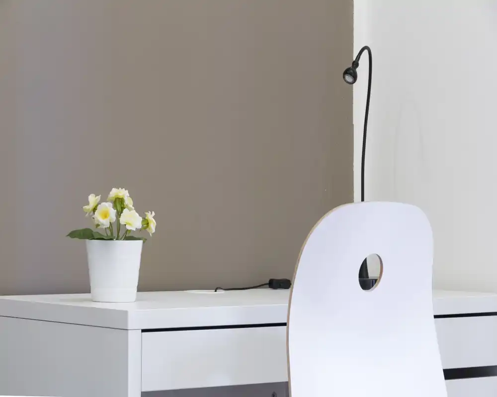 Angolo lavoro luminoso e minimale con scrivania bianca, sedia moderna e una piccola pianta in vaso; stile pulito e ispirazione scandinava, ideale per un angolo smart working.
