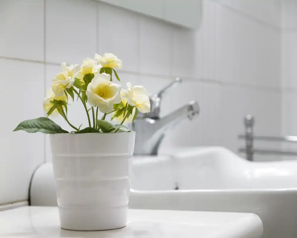 Area lavabo bagno luminosa e minimale con rubinetto cromato e vaso bianco con fiori che aggiunge un tocco decorativo fresco.