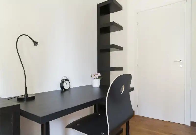 Rincón de oficina en casa minimalista con escritorio negro, silla a juego, estanterías, una lámpara pequeña y una planta — espacio de trabajo limpio y moderno ideal para concentrarse.