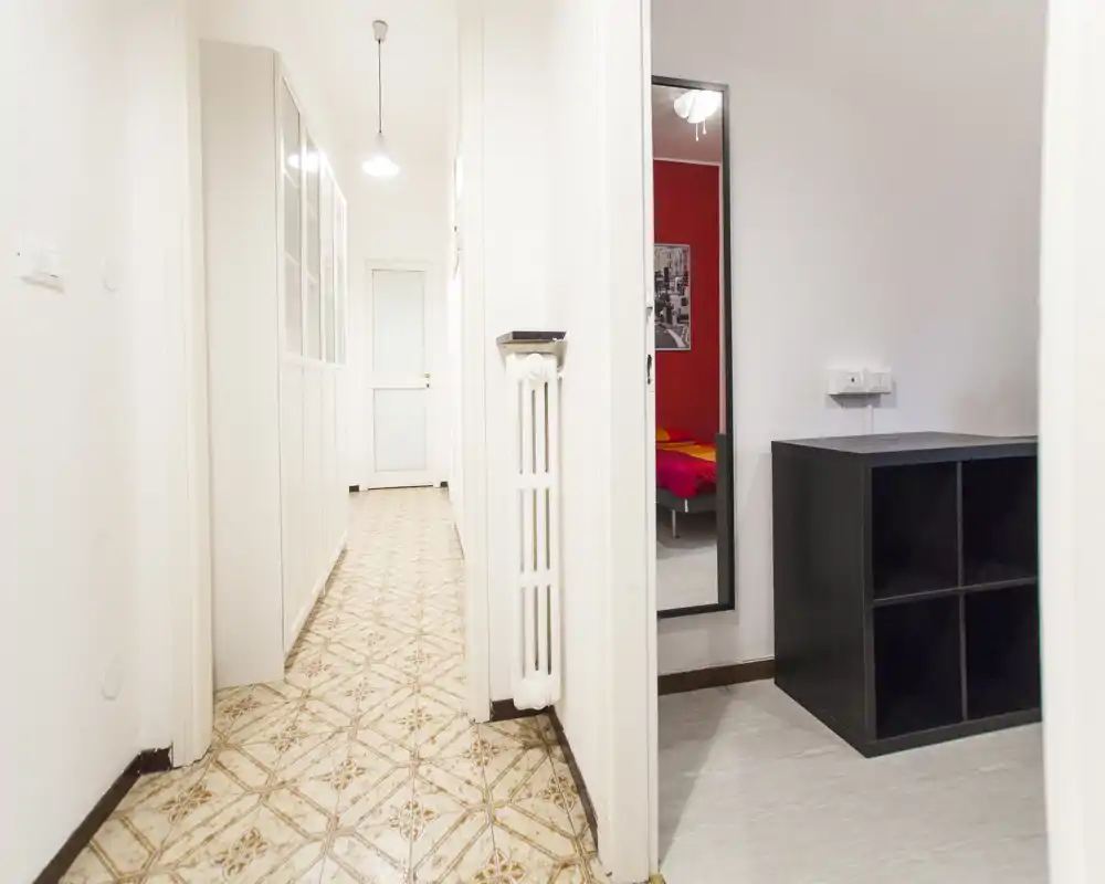 Corridoio luminoso e stretto con piastrelle decorative, radiatore a parete e porta che conduce alle stanze adiacenti; spazio pratico di passaggio.