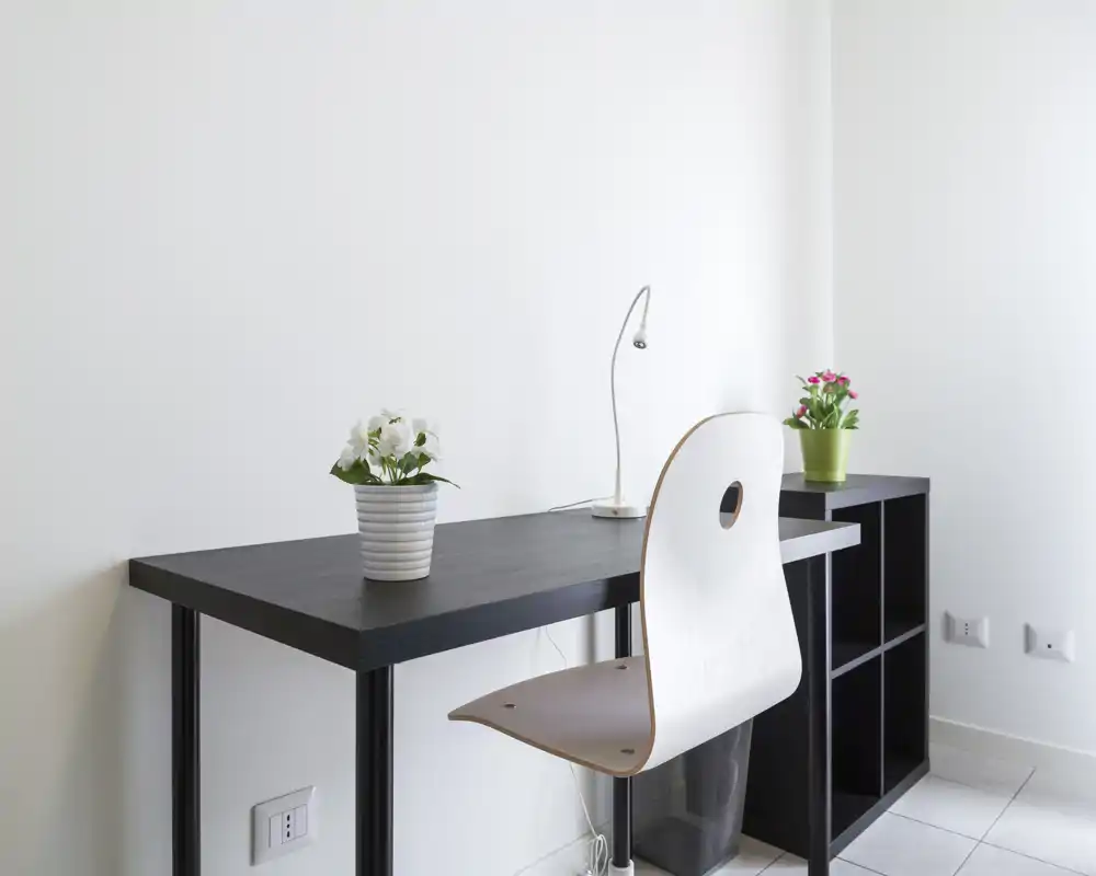 Spazio di lavoro luminoso e minimal con scrivania nera, sedia bianca e piccole piante in vaso — pulito, semplice e ben illuminato.