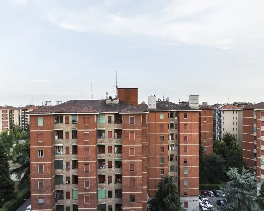 Vista esterna di un palazzo in mattoni rossi in un contesto residenziale urbano, ripreso dall'alto con edifici e alberi circostanti.