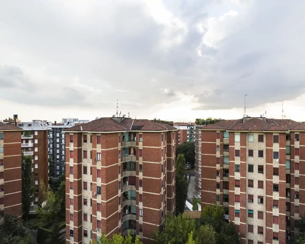 Vue extérieure sur la ville montrant plusieurs immeubles résidentiels de taille moyenne et des cimes d'arbres sous un ciel couvert — appropriée pour présenter la vue depuis un balcon ou un appartement.