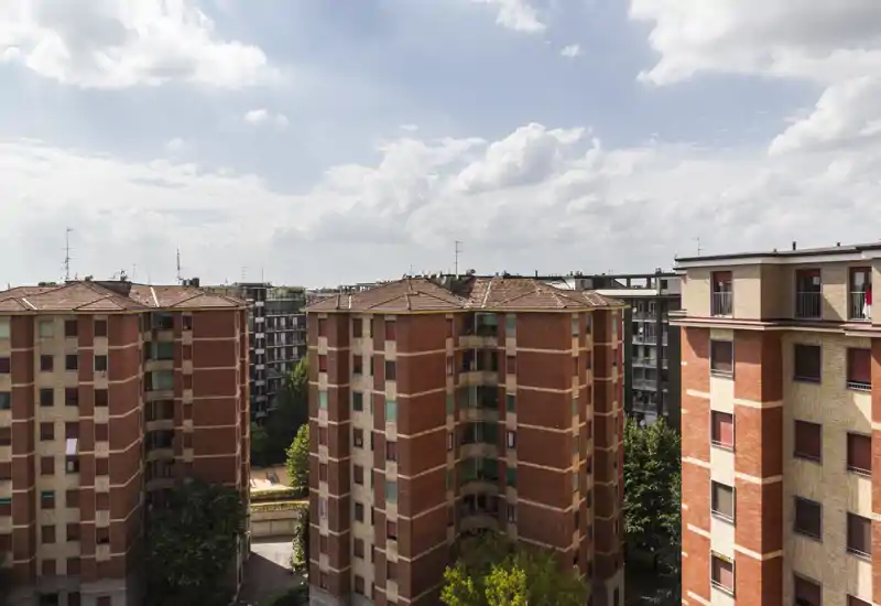 Exterior urban view showing multiple mid-rise apartment buildings under a partly cloudy sky; useful for listing the building’s façade and surroundings.
