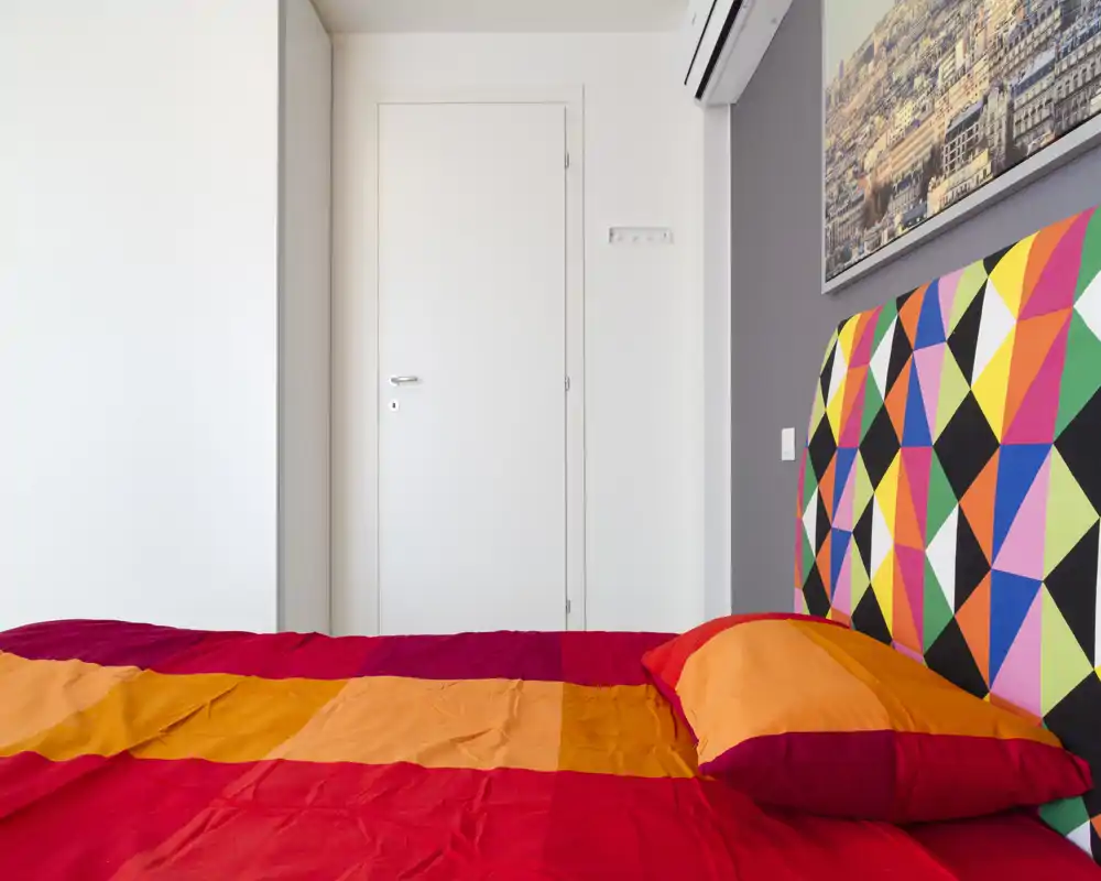 Chambre moderne et colorée avec une tête de lit géométrique et du linge lumineux. Le lit est au centre de l'image, la pièce est bien éclairée et soignée pour un séjour confortable.