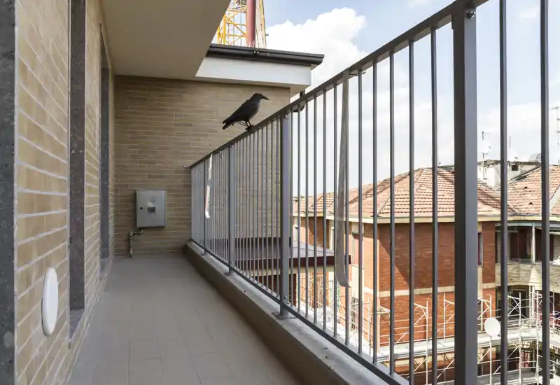 Balcón soleado con suelo de baldosa y barandilla metálica, con vistas a los tejados cercanos. Espacio exterior práctico, ideal para relajarse o colocar un pequeño asiento.