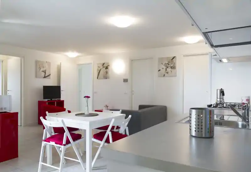 Open-plan living area with a small dining table, sofa and an integrated kitchen counter; bright, modern and neatly staged for short-term rental.