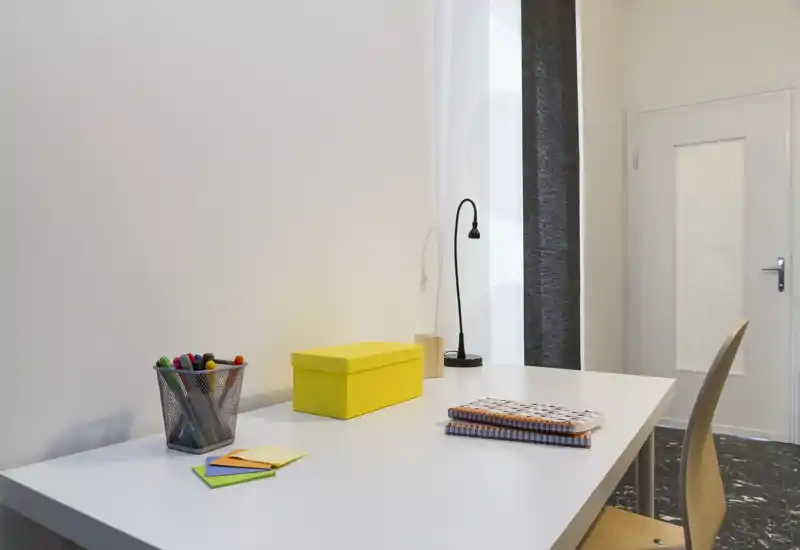 Espacio de trabajo luminoso y minimalista con escritorio blanco, silla, lámpara y material de papelería colorido — perfecto para estudiar o trabajar.