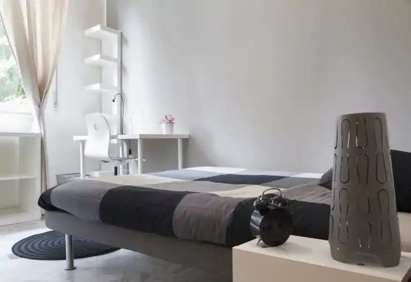 Camera da letto moderna e luminosa con letto matrimoniale, scrivania vicino alla finestra e arredi minimal: ideale per un soggiorno confortevole con luce naturale.