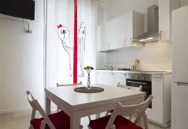 Cuisine moderne compacte avec four intégré, plaque de cuisson et petite table à manger aux chaises à coussins rouges ; style lumineux et minimaliste, idéal pour un appartement citadin cosy.