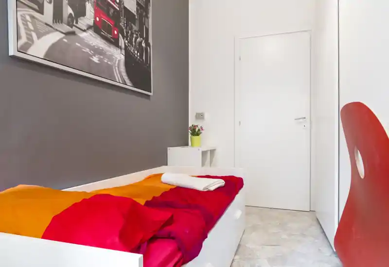 Dormitorio individual compacto y estiloso con ropa de cama naranja-roja, cama blanca moderna y decoración minimalista limpia, ideal para estancias individuales.
