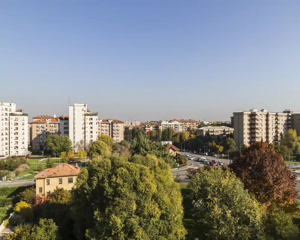 Panoramic outdoor view from a higher floor showing tree-lined green spaces, residential blocks and a clear sky — ideal to highlight the neighborhood and surroundings.
