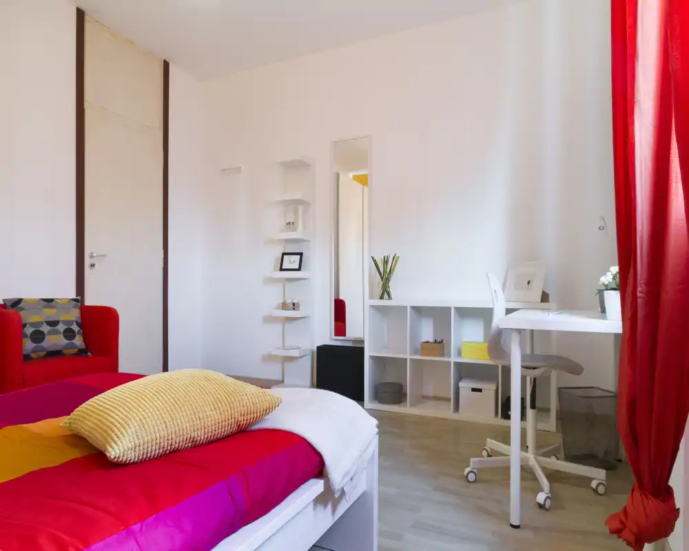 Bright, well-staged bedroom with a colorful bed, cozy textiles and a tidy workspace by the window — ideal for rental listings highlighting comfort and natural light.
