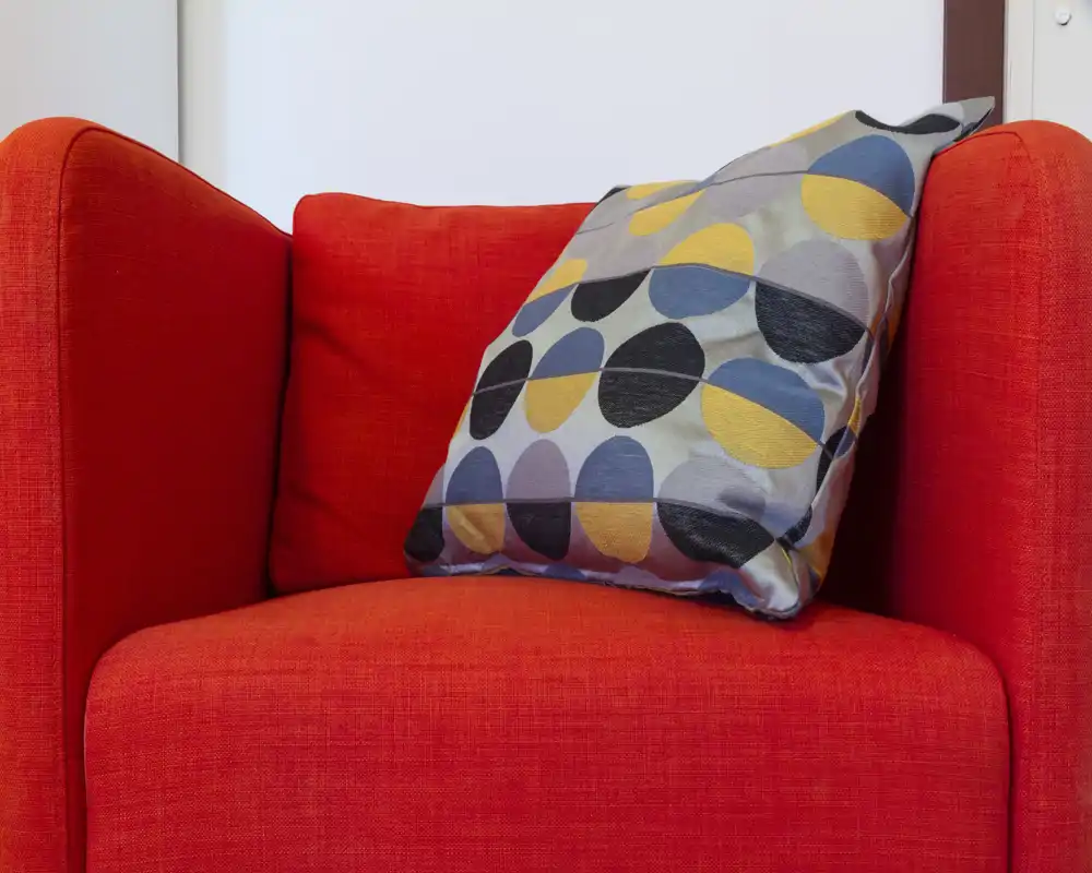 Close-up of a vibrant red armchair with a colorful patterned cushion, presenting a cozy and stylish living area accent.