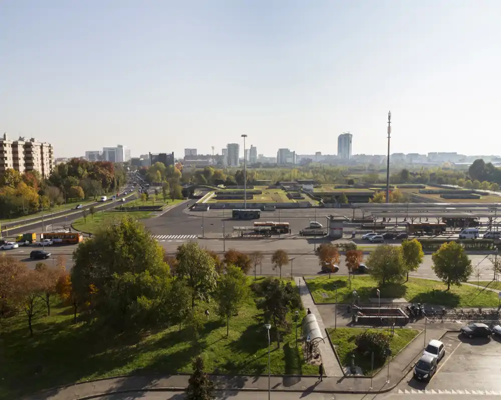 Vista esterna soleggiata su un parco e le strade adiacenti con autobus e lo skyline cittadino in lontananza — ottima per mostrare il quartiere e i collegamenti.