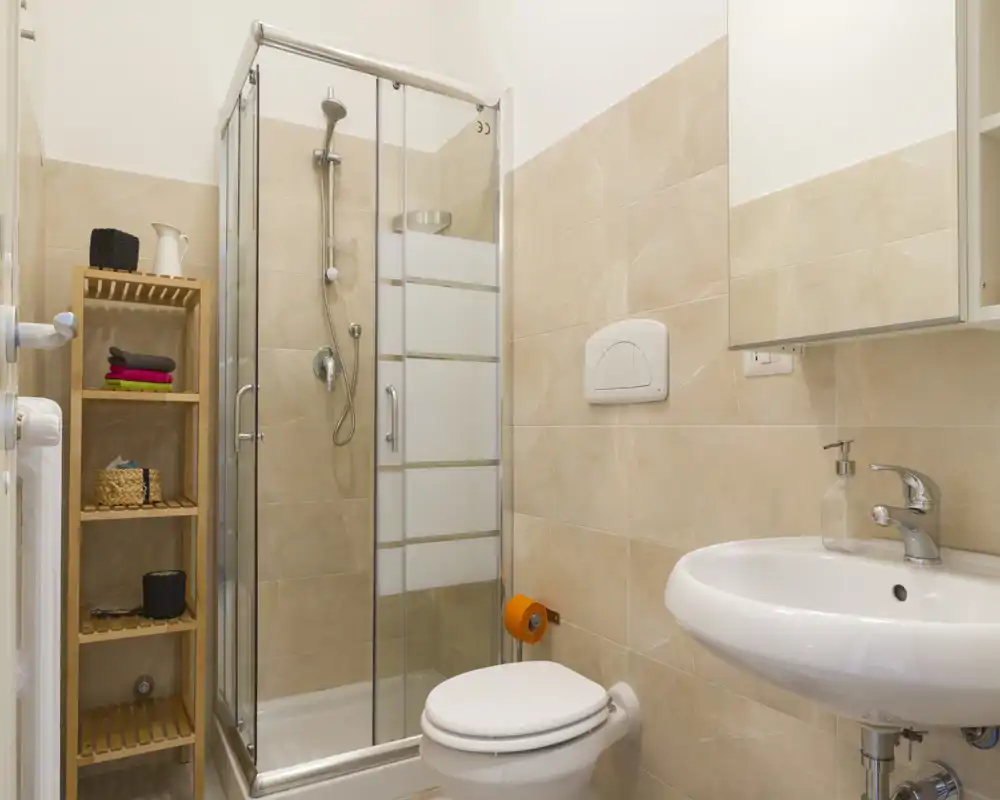 Bagno moderno e luminoso con doccia in vetro, wc a parete e lavabo con specchio: scaffalatura ordinata per spazio extra di conservazione.