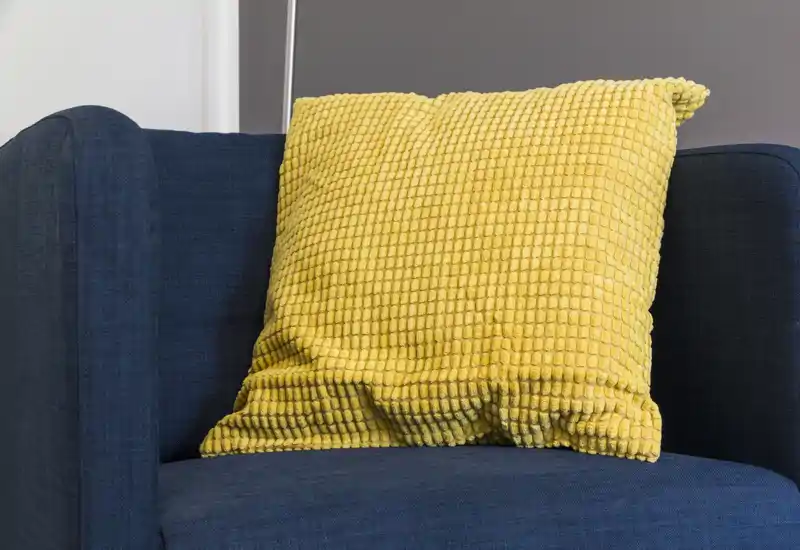 Close-up of a blue upholstered armchair with a textured yellow cushion, showing a cozy seating detail and color contrast ideal for living room listings.