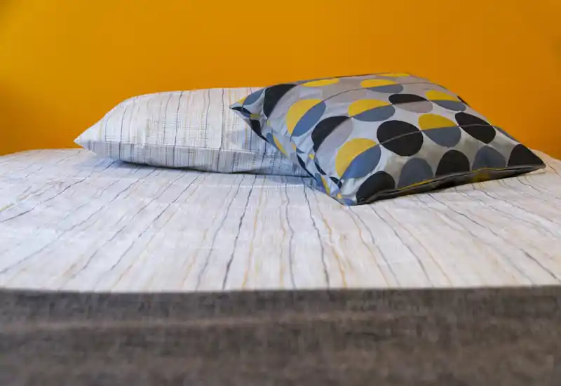 Toma luminosa y bien presentada de un dormitorio, con cama hecha y cojines estampados frente a una pared naranja intensa.