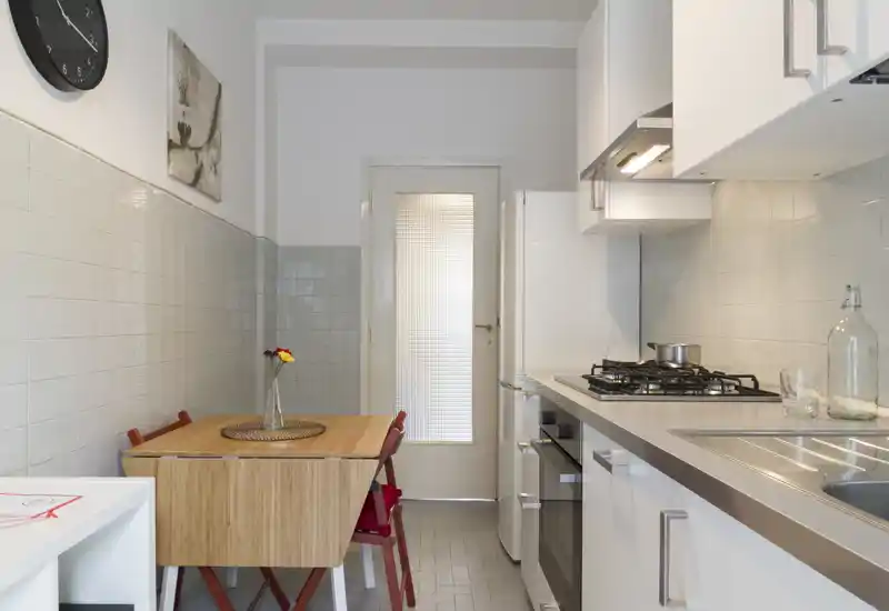 Compact, modern kitchen with a gas hob, integrated oven and a small wooden dining table with chairs — bright, clean and efficiently organized for a city apartment.