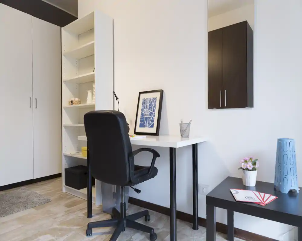 Angolo ufficio domestico minimal e luminoso con scrivania bianca, sedia girevole, scaffali e armadio — spazio ordinato ideale per il lavoro da remoto.