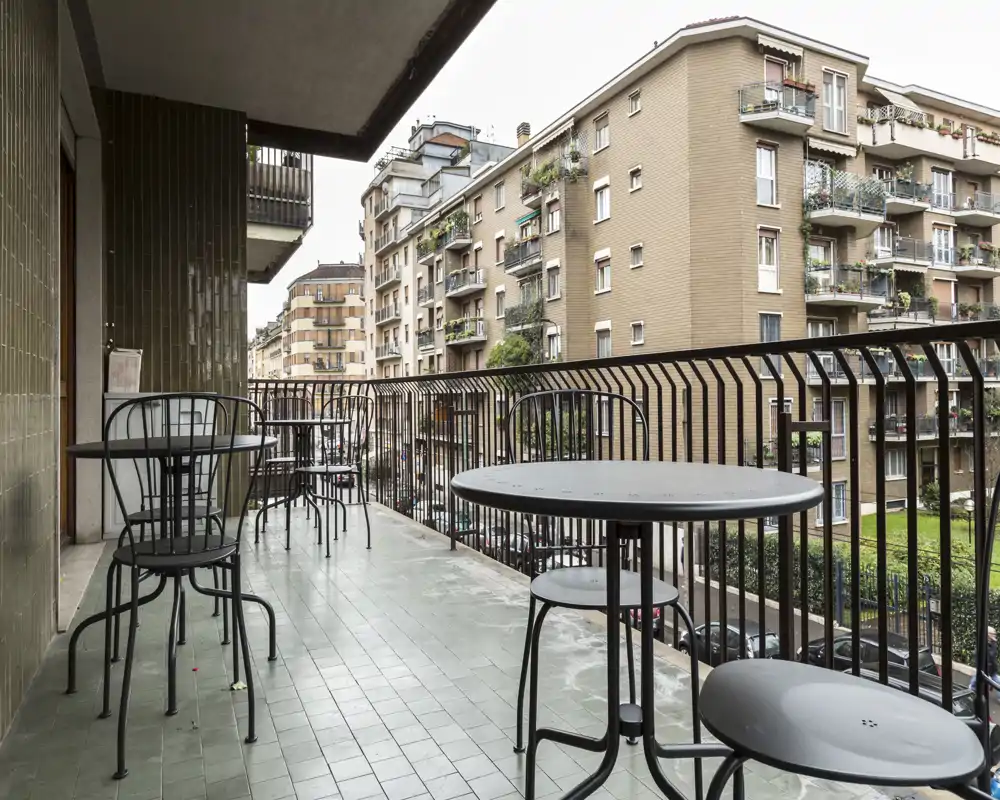 Balcone con tavolini e sedie in metallo che si affaccia su una strada residenziale — ideale per un caffè mattutino o come spazio di lavoro all'aperto.