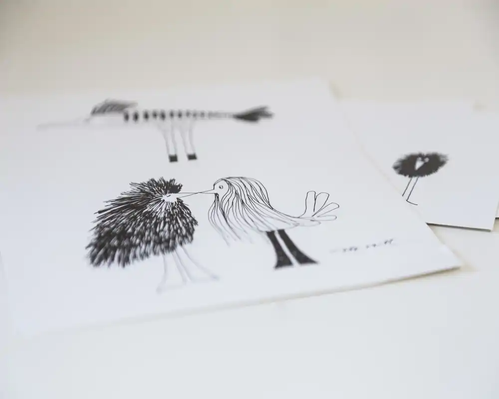Close-up of black-and-white ink drawings on paper featuring stylized birds; minimal background and shallow depth of field.