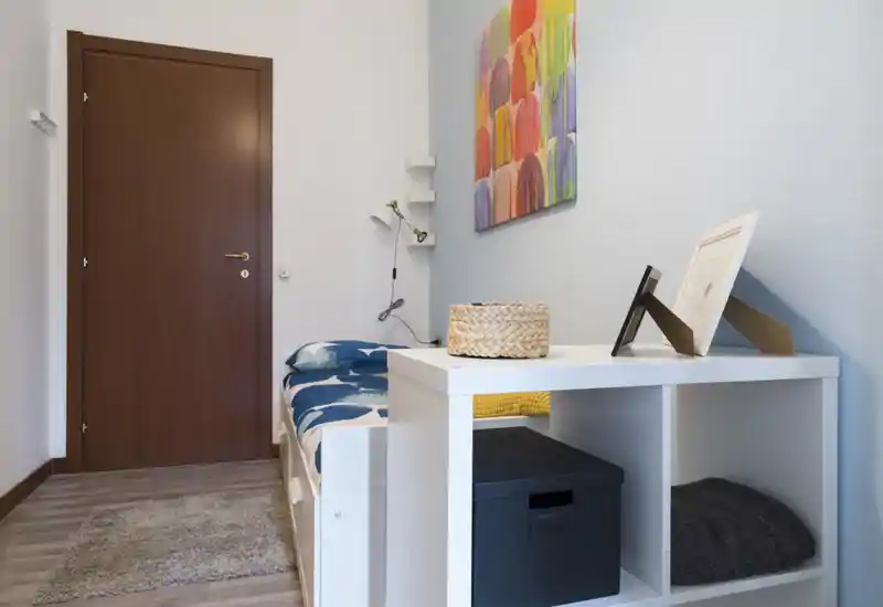 Compact single bedroom with a neat daybed, storage shelving and a colorful wall painting; clean, well-lit and styled for a cozy stay.