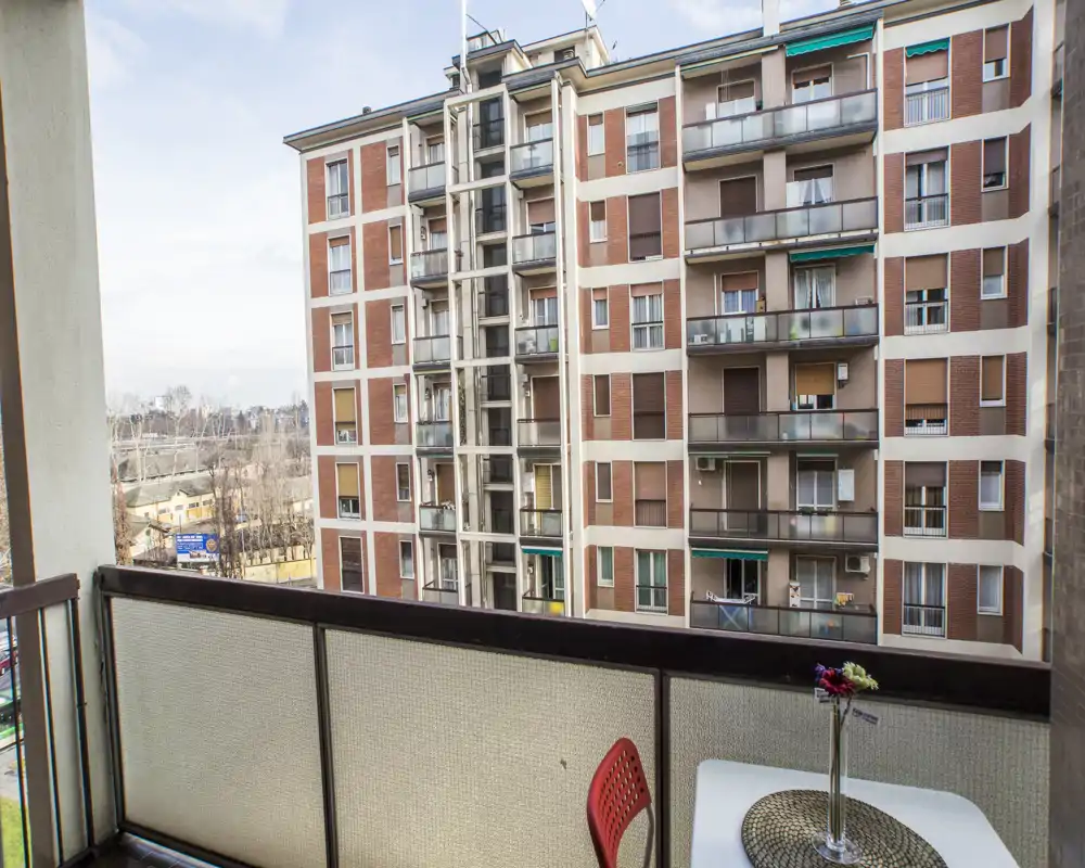 Balcon ensoleillé avec petite table, une chaise et rambarde donnant sur des immeubles voisins — parfait pour un café du matin avec vue sur la ville.