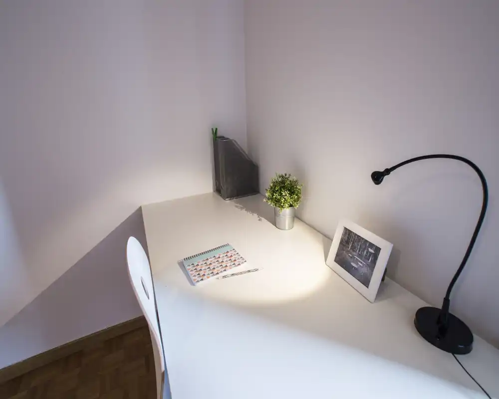 Coin bureau soigné et minimaliste avec bureau blanc, lampe de travail, petite plante et photo encadrée — parfait pour étudier ou travailler à distance.