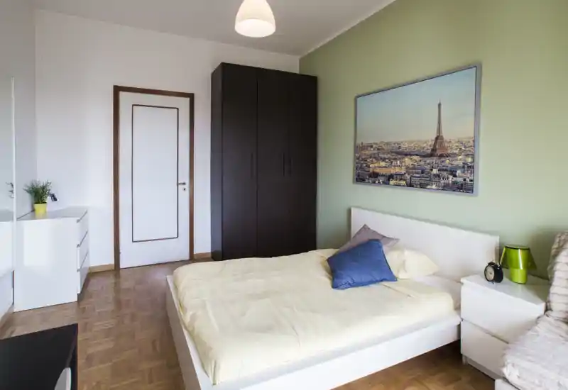 Chambre lumineuse et bien rangée avec un lit double, table de chevet et armoire ; linge de lit neutre et tableau encadré créent une ambiance apaisante.
