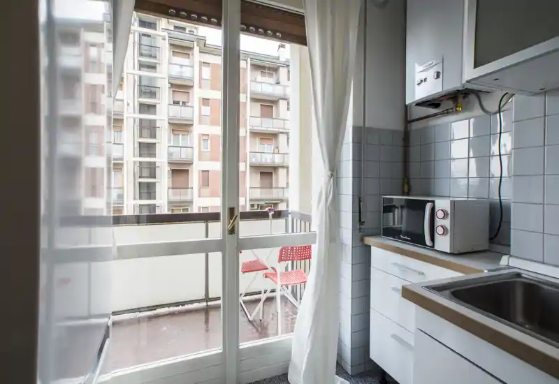 Compact kitchen with a sliding glass door leading to a small balcony. The layout includes a sink, countertop, microwave and tiled backsplash, with plenty of natural light.