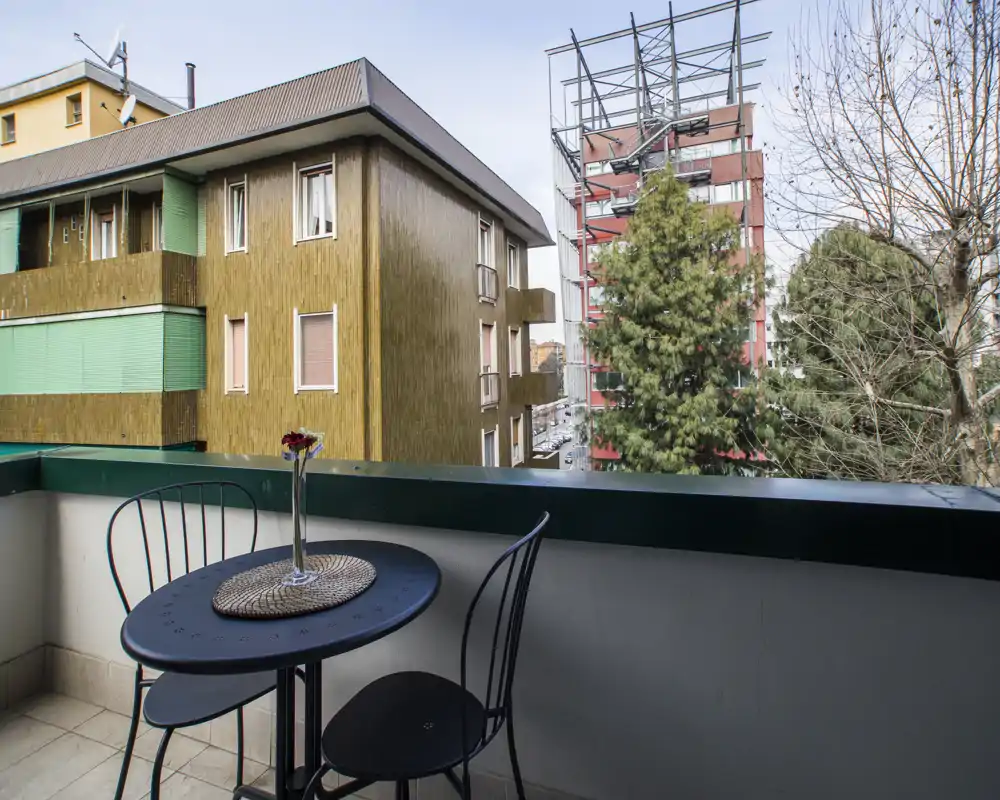 Piccolo balcone arredato con un tavolino bistro e due sedie, con vista su edifici e alberi — ideale per il caffè mattutino.