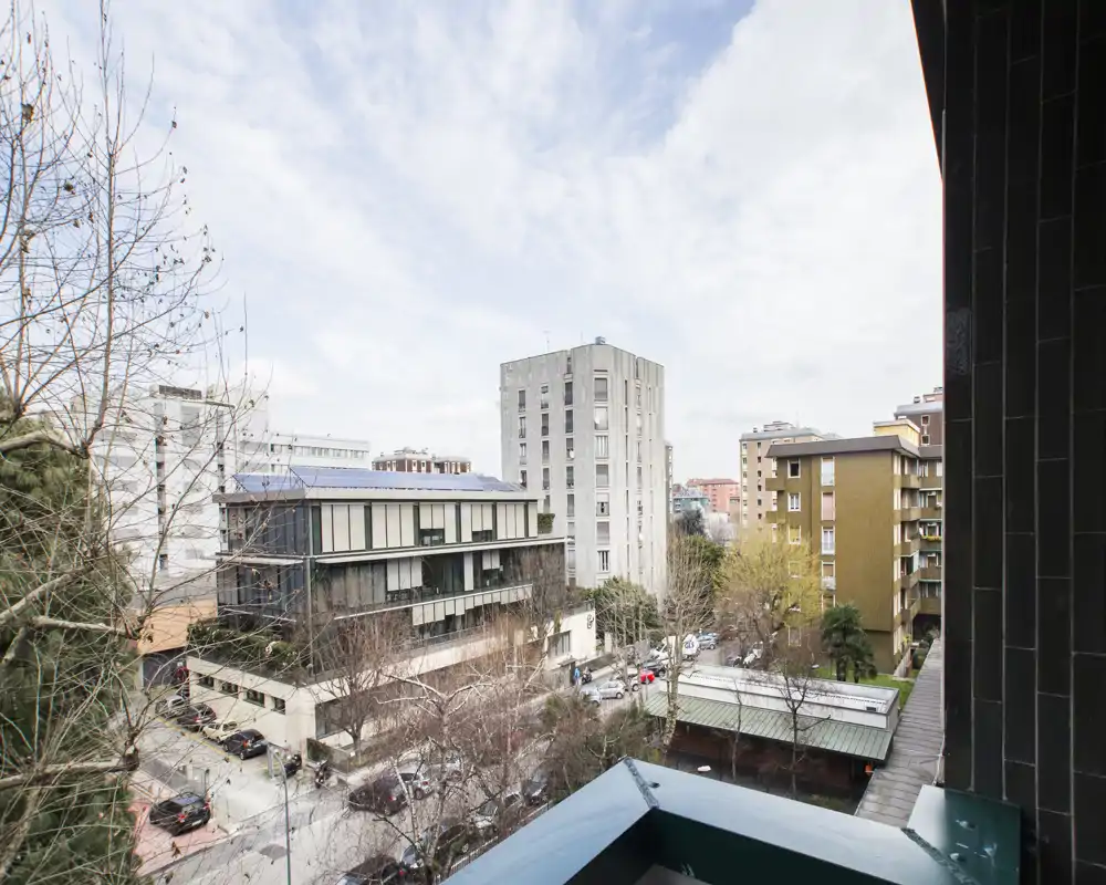 Vista dal balcone su una strada cittadina con palazzi residenziali e alberi, che offre una luminosa prospettiva urbana.