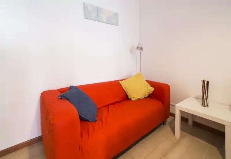 Compact living area with a bold red sofa, cozy cushions and a small side table under soft warm lighting — ideal for relaxed evenings.