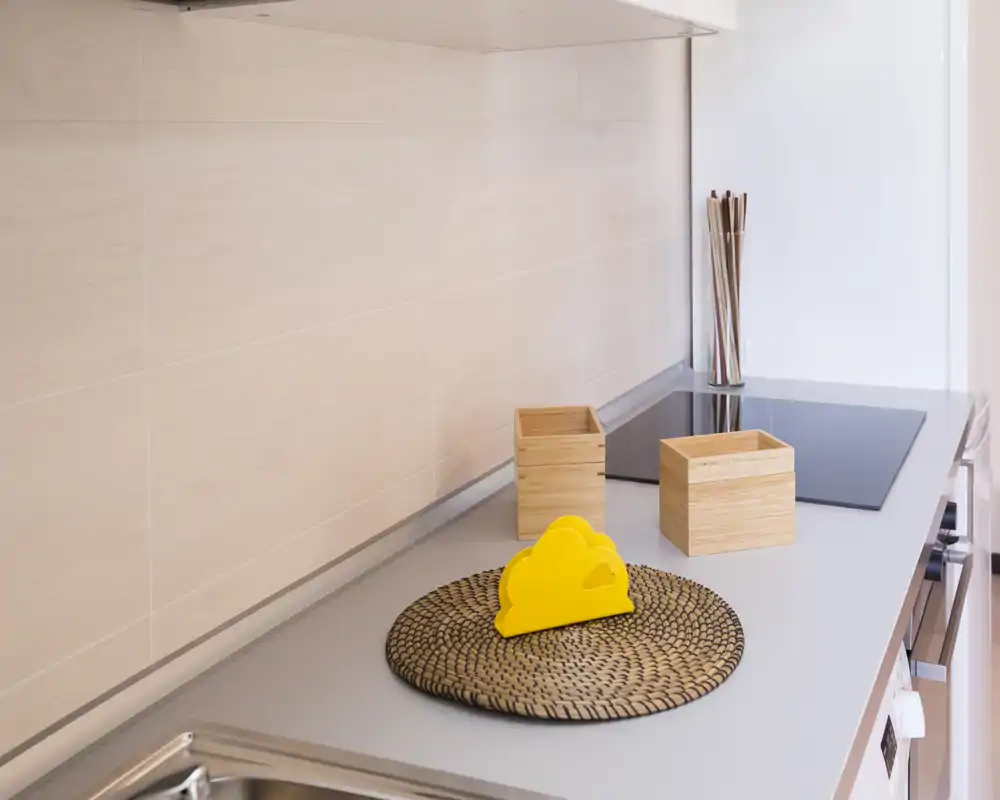 Encimera de cocina luminosa y minimalista con placa de inducción, cajas de madera decorativas y un salvamanteles tejido — zona de preparación limpia y moderna.