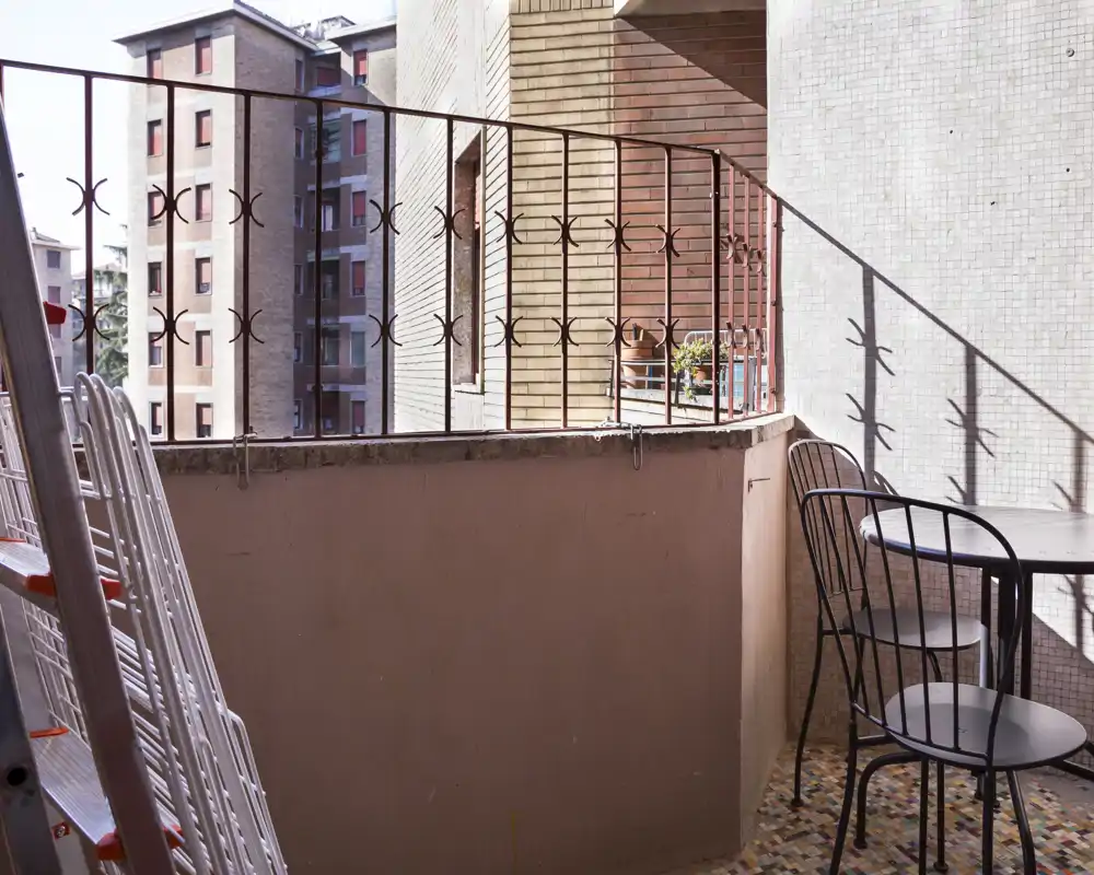 Pequeño balcón soleado con barandilla de hierro forjado, suelo de mosaico y una mesa bistró con dos sillas — ideal para el café de la mañana.