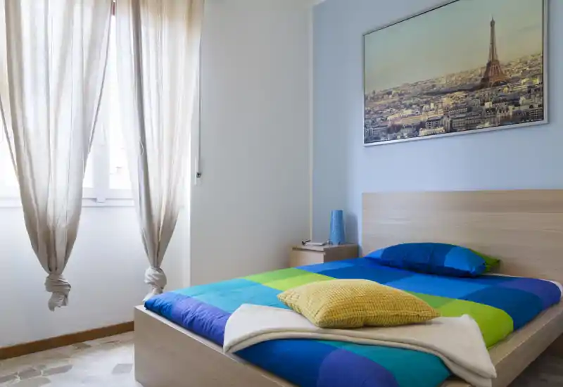 Dormitorio luminoso y ordenado con una cama individual colorida, mesita de noche y luz natural desde la ventana—decoración moderna y minimalista, ideal para alquileres de corta estancia.